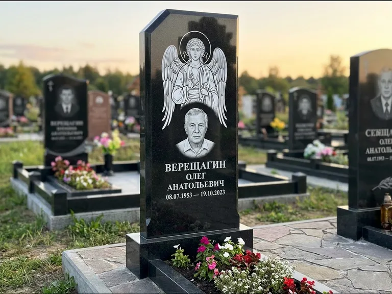 Памятник с гравировкой иконы: стела с резным навершием и нимбом в золоте — гравировка образа Спасителя, высокие разросшиеся туи полукругом, работа «Мельникова» в Рязани