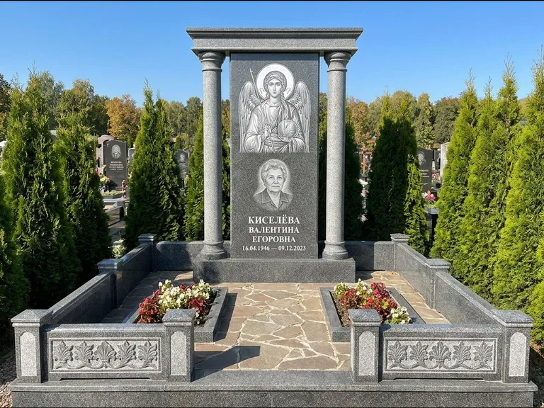 Памятник с гравировкой иконы: массивная стела с двускатным навершием-домиком — гравировка Николая Чудотворца, живая изгородь из туи, работа «Журавлёв» в Рязани