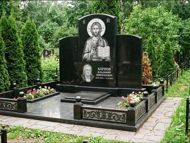 Памятник с гравировкой иконы: широкая панорамная стела с золочёным нимбом — гравировка образа Матроны Московской, цветник с белыми хризантемами, работа «Мельникова» в Рязани
