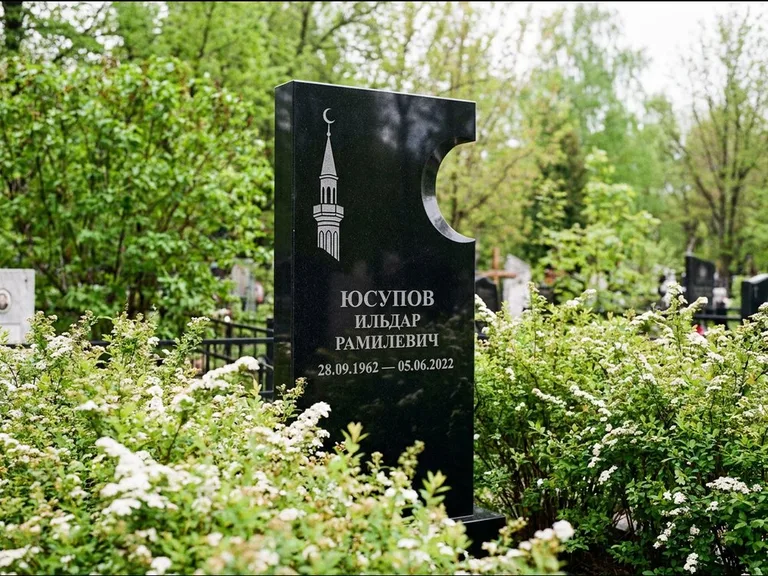 Мусульманский памятник с гравировкой мечети: стела с боковым вырезом в форме полумесяца — гравировка минарета с полумесяцем, низкие кусты спиреи в цвету, работа «Юсупов» в Рязани